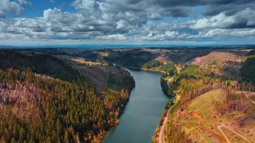 Grey river reflecting the cloudy sky crosses the mountainous area.