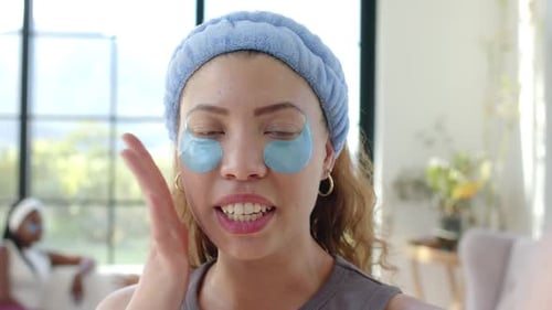 Mujeres afroamericanas, un tutorial sobre cómo mirar mientras usan parches azules de hidrogel en la sala de estar
