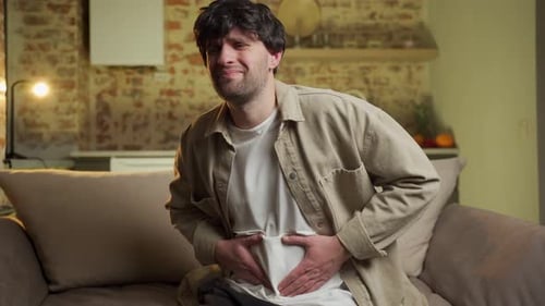 Man Holding Stomach in Pain on Couch