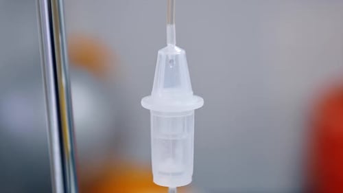 Liquid medicines slowly dripping inside the reservoir of drop counter. Medical equipment close up.