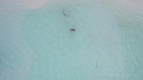 young couple in swimwear walking through crystal clear blue water on sandbar towards a beach, aerial