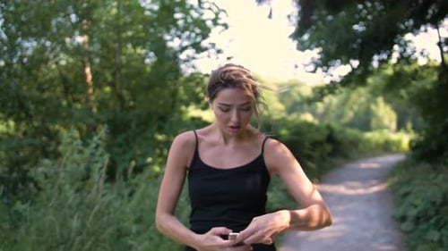 Young woman jogging on a path in a park stops to answer a call on her cell phone. Talking and smilin