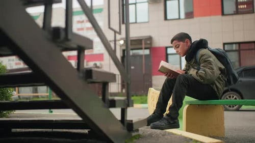 Boy Sitting Outdoors Reading Book With Concentration