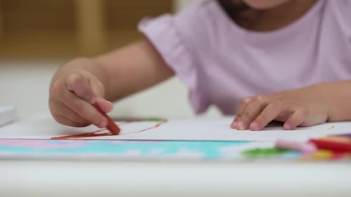 Nahaufnahme eines Mädchens im Vorschulalter, das zu Hause mit bunten Ölpastellen auf Papier zeichnet und malt