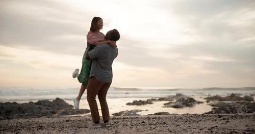 Sunset, couple hug and love at a beach with kiss, support or lifting in celebration in seaside