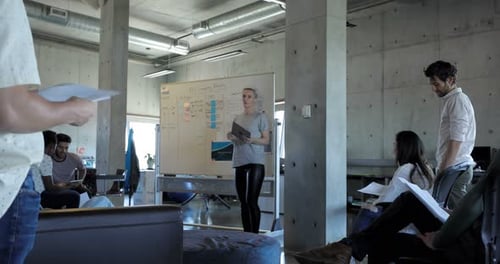 Businesswoman leads team brainstorming ideas at whiteboard in bright modern office
