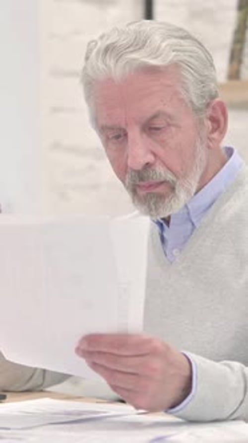 Senior Man Reviews Documents and Laughs in Office