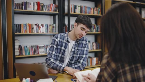 Étudiant étudiant dans une bibliothèque tout en discutant d'un projet avec un pair assis à une table en bois
