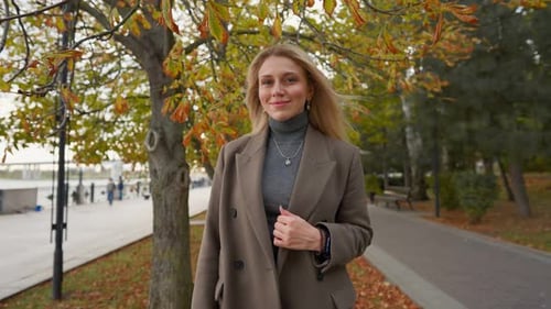 Attractive Business Woman with Blond Hair Walks in Autumn Park on Cloudy Day