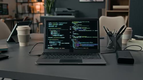 Desk with Grey Laptop Displaying Code, Black External Hard Drive Connected to It