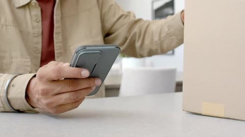 Holding smartphone, man checking package delivery status at home table