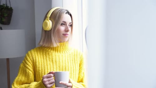 Woman Listens with Headphones Holding Mug Indoors