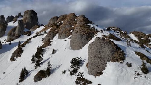 Vue aérienne des montagnes enneigées de Ciucas avec des sommets escarpés sous un ciel nuageux, fin de l'hiver