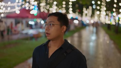 Asia man an wearing glasses walking forward in Night City with Bokeh Neon Street Lights