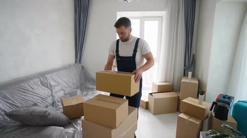 Man Stacking Cardboard Boxes in Brightly Lit Living Room
