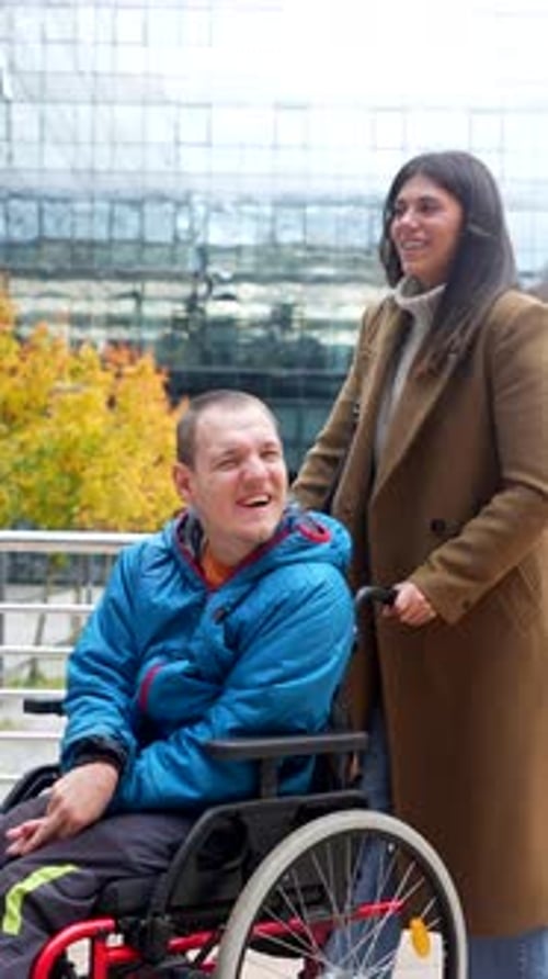 Woman pushing man in wheelchair on city street