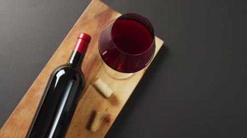 Red wine glass, bottle and cork lying on wooden board with copy space on black background
