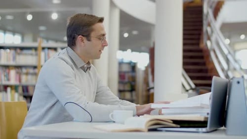 Focused Man Sitting at Desk and Writing in Library