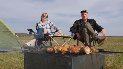 Pareja divirtiéndose acampando mientras asa carne en la barbacoa