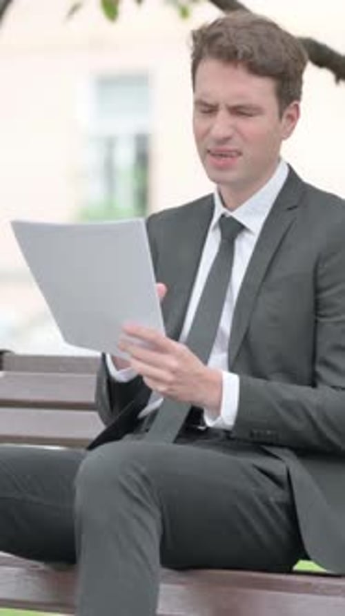Serious Man in Suit Reads Documents on Bench