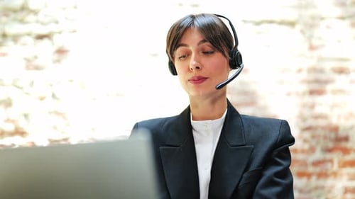 Businesswoman in Headset Works on Laptop in Office Communicating Effectively