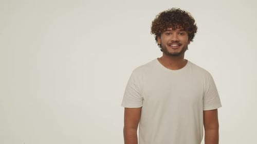 Front View of Laughing Young Man Pointing with Finger to the Side Curly Guy in White Tshirt Posing