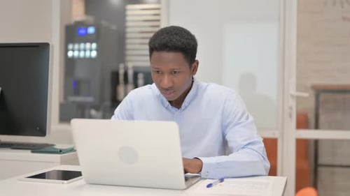 African Businessman Looking at Camera while Working on Laptop in Office