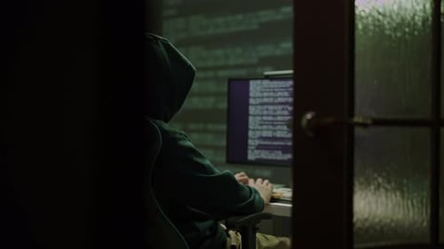 Personne cagoulée tapant sur le clavier de l'ordinateur dans une pièce sombre en se concentrant sur l'écran affichant des lignes de Code