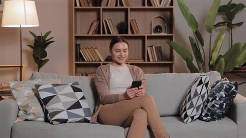 Woman Relaxing on Sofa Using Smartphone Indoors