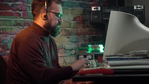 Mann arbeitet an einem Desktop-Computer aus den 1980er Jahren und hört Musik mit Kopfhörern auf dem Kopf