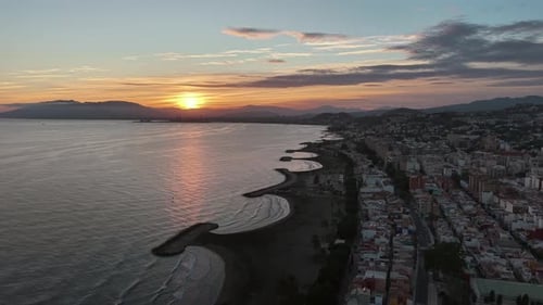 Aerial view of a coastal city at sunset with curved beaches, calm sea and dense urban skyline