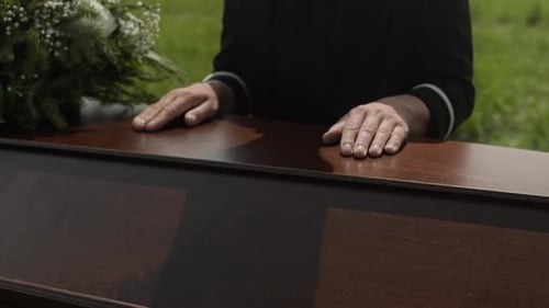 Woman Grieving Over Casket Outdoors Next To Flowers