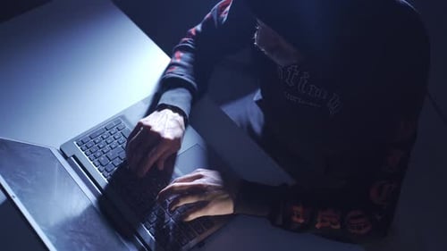 Ein Hacker-Mann in schwarzem Hoodie arbeitet in einer Dunkelkammer, knackt Passwörter und hackt Websites.