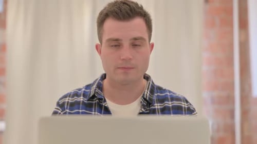 Close up of Young Man Working on Laptop Looking at Camera