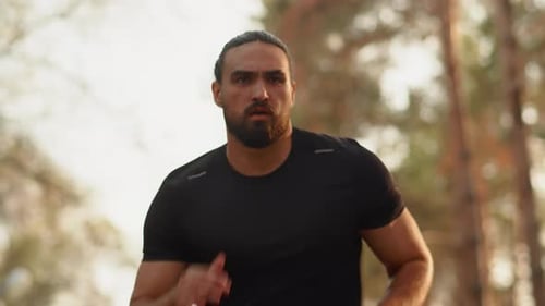 Young Muscular Athlete Close Up Running Fast with a Confident Look Ahead in an Alley of a City Park