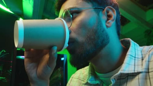 Man Drinking Coffee at Computer in Green Lit Room