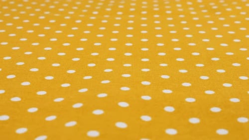 Close-up view of the amber yellow with white polka dots cotton fabric rotated on the display case.