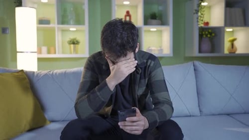 Sad Young Adult Looking at Phone on Couch