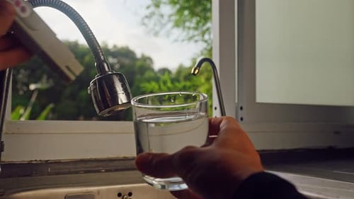 Vue à la première personne de la main utilisant un testeur numérique de qualité de l'eau dans un verre d'eau douce dans une cuisine à proximité