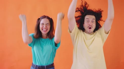 Two Vibrant Young Adults Express Their Enthusiasm Against a Lively Orange Background Capturing a