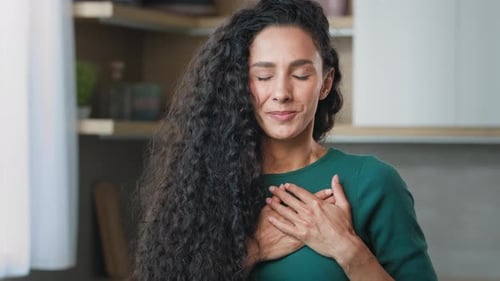 Joven chica rizada hispana, franca, mujer honesta, de pie, en el interior, coloca las palmas dobladas