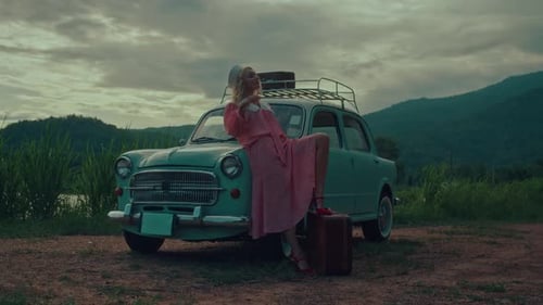 Ein Mädchen in einem Vintage-Kleid lehnt sich auf ein türkisfarbenes Retro-Auto vor dem Hintergrund der Berge