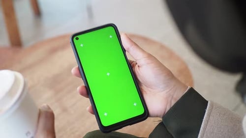 Holding a Smartphone with a Green Screen in a Cozy Cafe