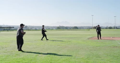 Responding to coach signal, male gloved teammates practicing relay throws across outfield and mound