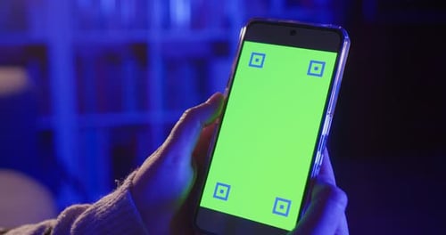Mujer que sostiene un teléfono inteligente en casa por la noche