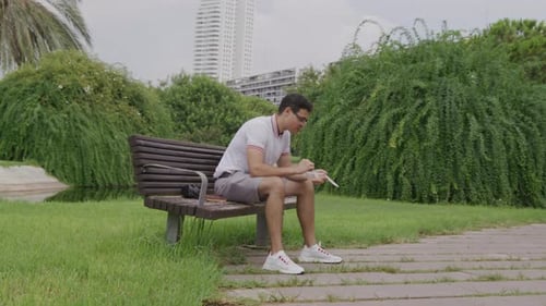 Young Male Tourist Having Lunch While Sitting in Lush Park Outdoors