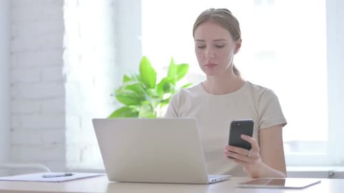 Woman Using Smartphone and Laptop at Desk