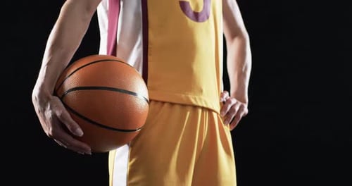 Female basketball player in a basketball uniform holds a ball on a black background