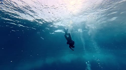 Solitary scuba diver descends through crystal clear sapphire depths towards a mysterious ocean