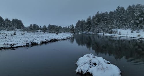 An Aerial View of a Frozen River Flowing Through Snowcovered Forests on a Cloudy Sunset Sky